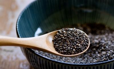 A wooden spoon full of chia seeds above a bowl