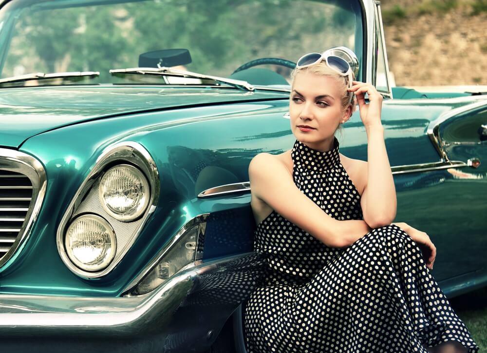 woman in polka-dotted dress sitting next to vintage car