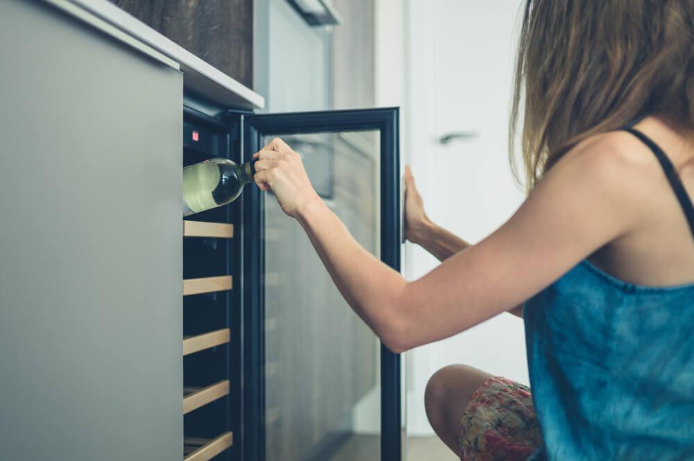 Woman taking bottle of wine from wine cooler