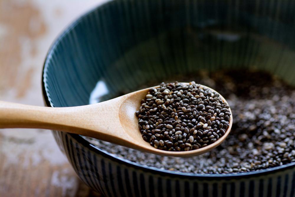 A wooden spoon full of chia seeds above a bowl