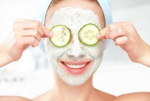 Woman puts cucumbers on eyes while wearing facial mask