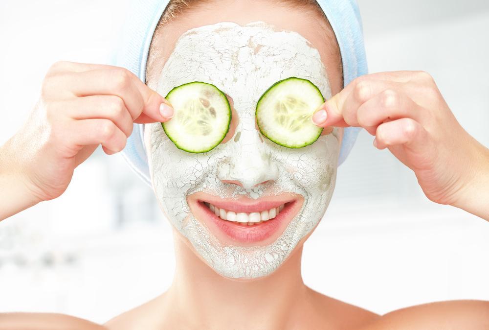 Woman puts cucumbers on eyes while wearing facial mask