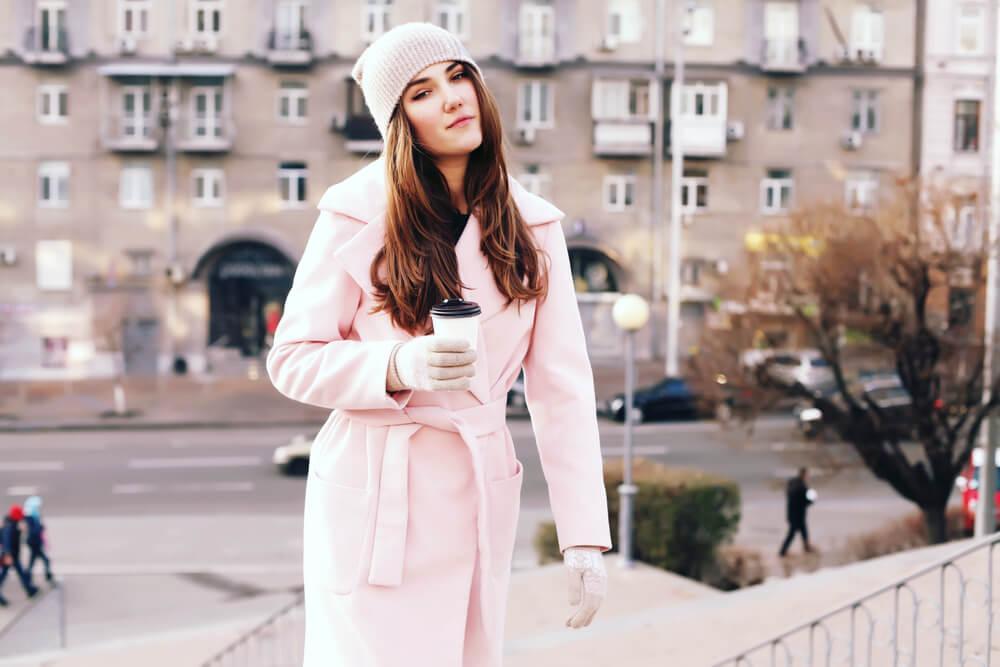 woman in pale pink coat with coffee cup