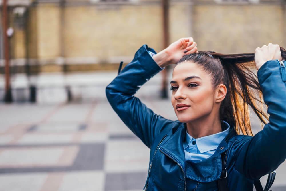 Woman tying her hair up in a ponytail 