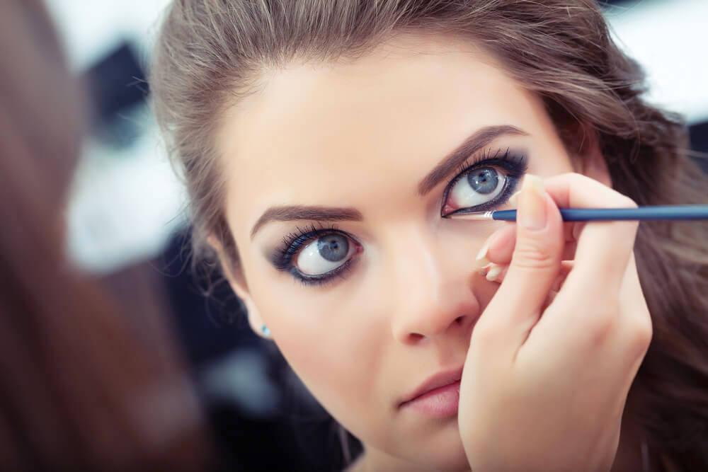 Makeup artist applying white eyeliner on model's eyes