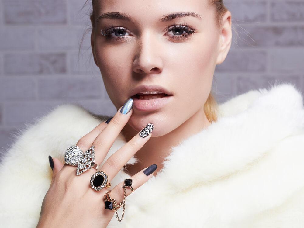 Fashionabel woman in white fur collar, with multiple rings and fashionable silver nail art