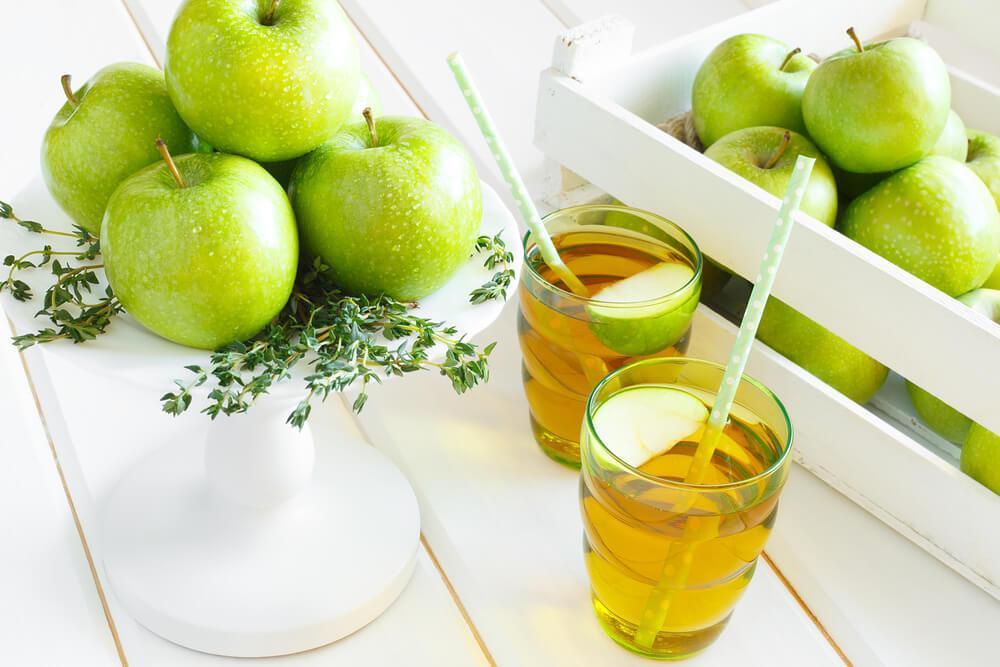 Two glasses of apple juice, with whole green apples 