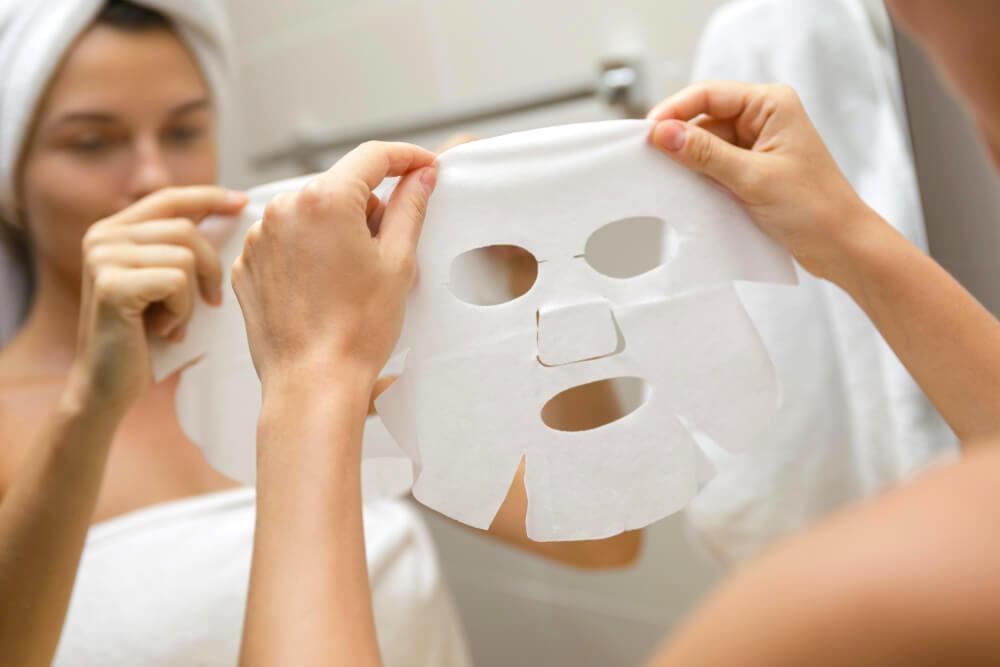 Woman applying sheet mask in bathroom